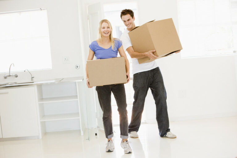 Couple carrying boxes moving into new home smiling